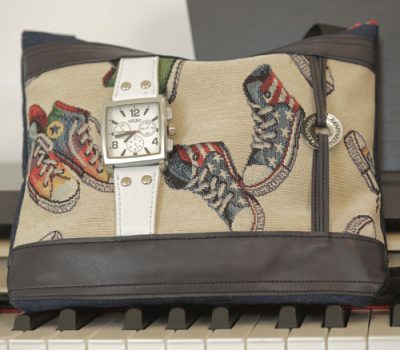 Sac qui donne l'heure en tissus beige avec des illustrations de chaussures haute maintenu par une structure en cuir avec des lacets en cuir pour maintenir le logo, une montre en cuir blanc et un cadrant carré blanc