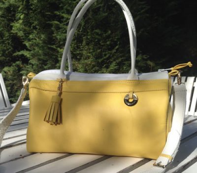 Sac complice en cuir jaune avec des bandes de cuir blanches, un porte clé jaune et le logo akapparence suspendu par un lacet jaune